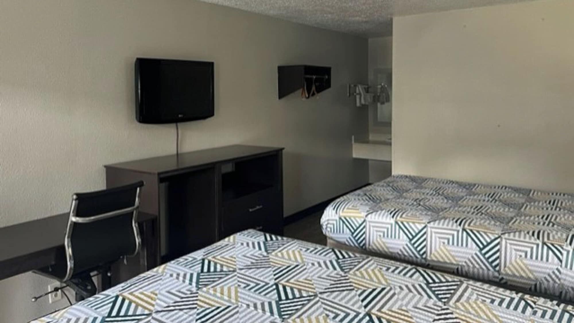A hotel room with two beds, a desk, a chair, a TV, and a mirror.