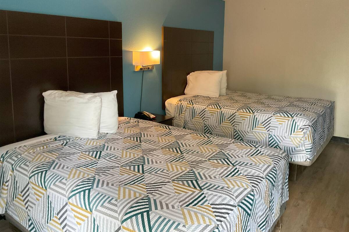 A hotel room with two beds, each with patterned bedding, a nightstand, a wall-mounted lamp, and a telephone.