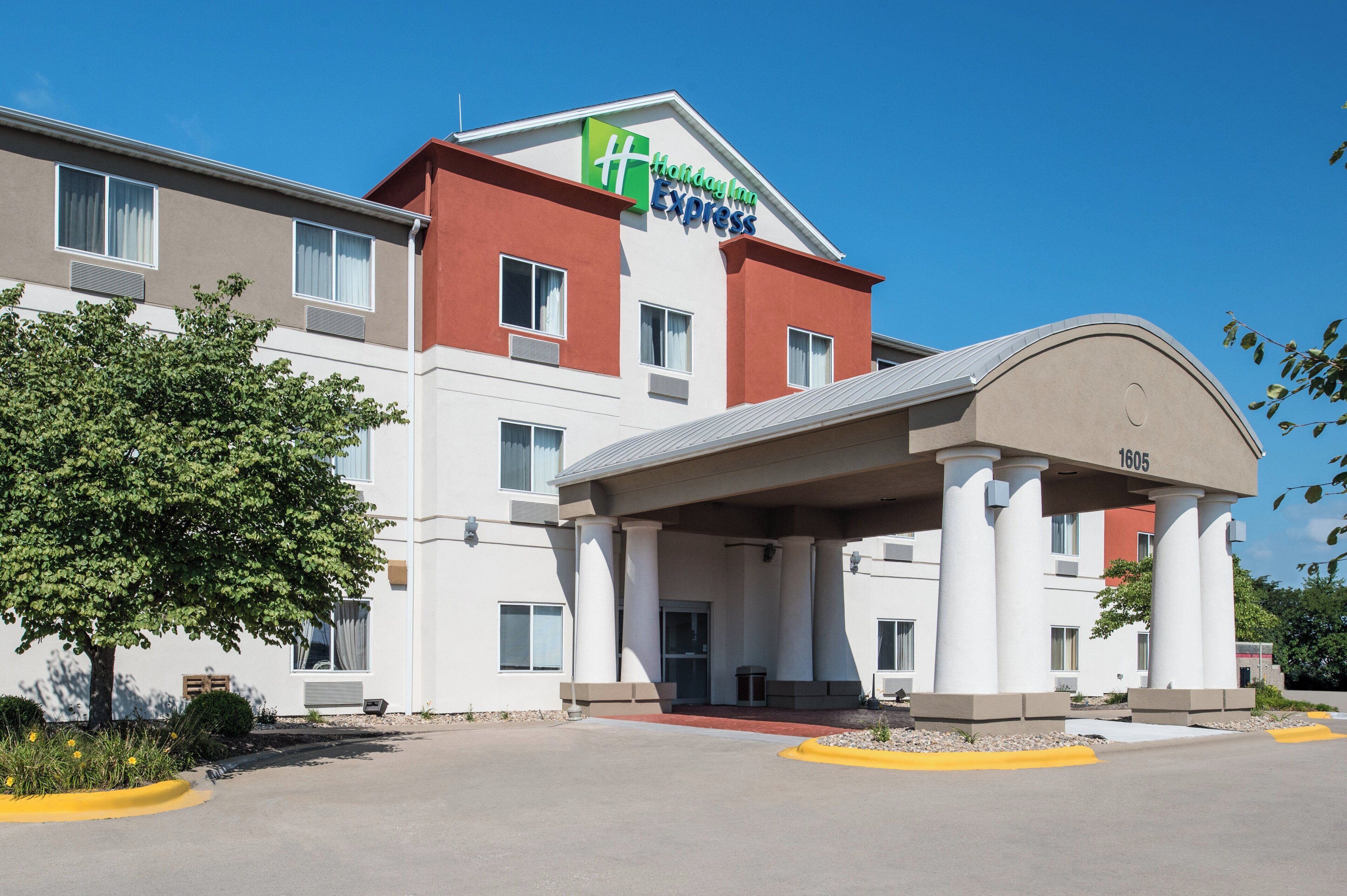 Un hotel Holiday Inn Express con un diseño moderno, que cuenta con una entrada destacada y un cielo azul despejado.