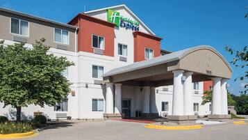 Un hotel Holiday Inn Express con un diseño moderno, que cuenta con una entrada destacada y un cielo azul despejado.