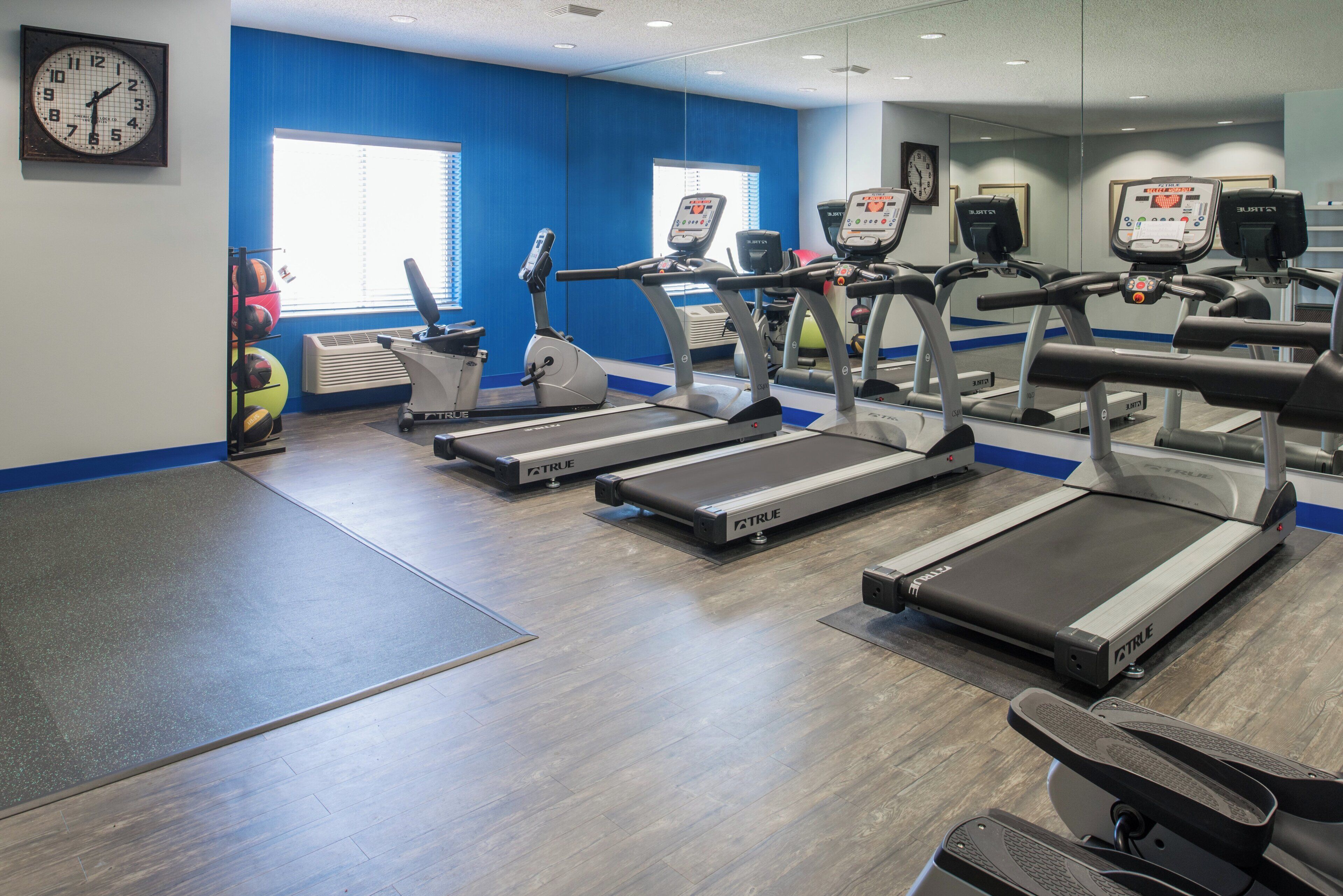 A gym with treadmills, exercise balls, and a clock on the wall.