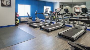 A gym with treadmills, exercise balls, and a clock on the wall.