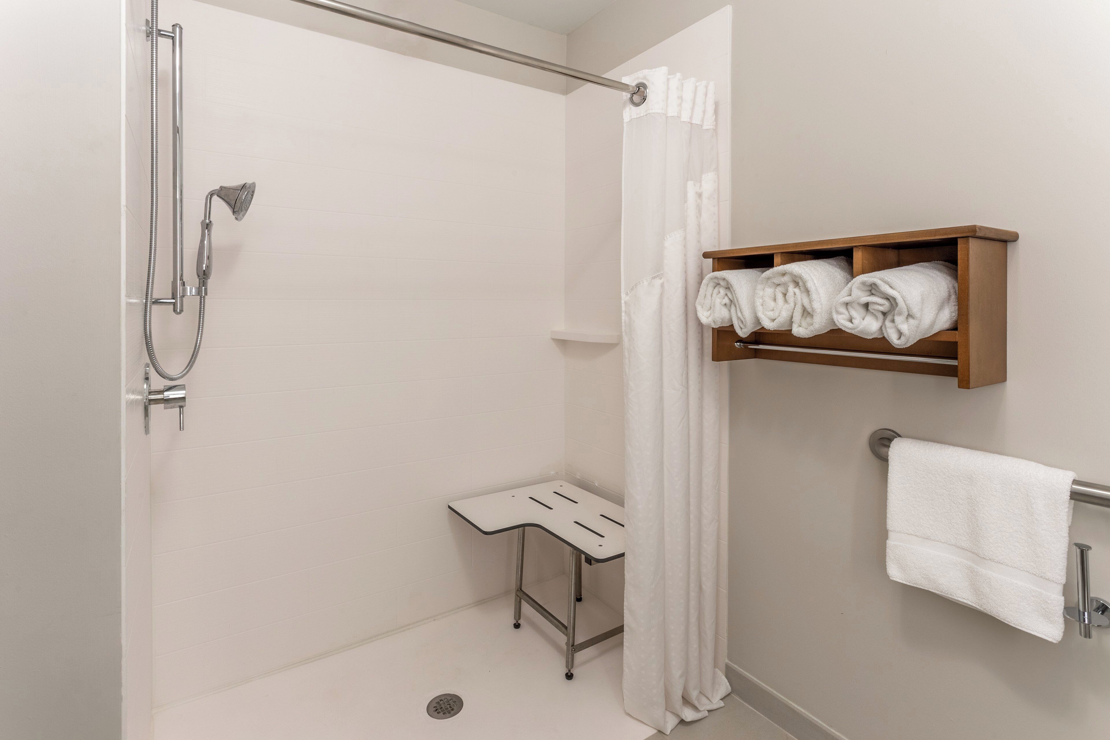 A shower with a handheld showerhead, a small stool, and a towel rack with a rolled towel.
