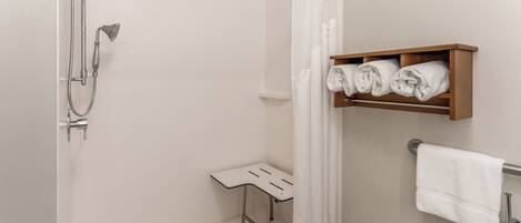 A shower with a handheld showerhead, a small stool, and a towel rack with a rolled towel.