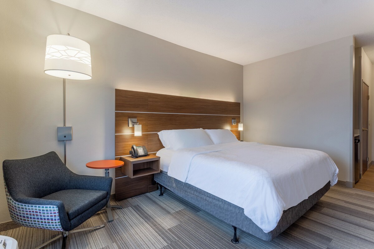 Une chambre d’hôtel avec un lit, une chaise, une table de chevet avec un téléphone et une lampe.