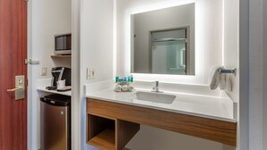 Un baño moderno con un lavamanos blanco, un espejo y una cafetera sobre una repisa.