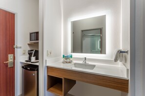 Une salle de bain moderne avec un lavabo blanc, un miroir et une machine à café posée sur une étagère.