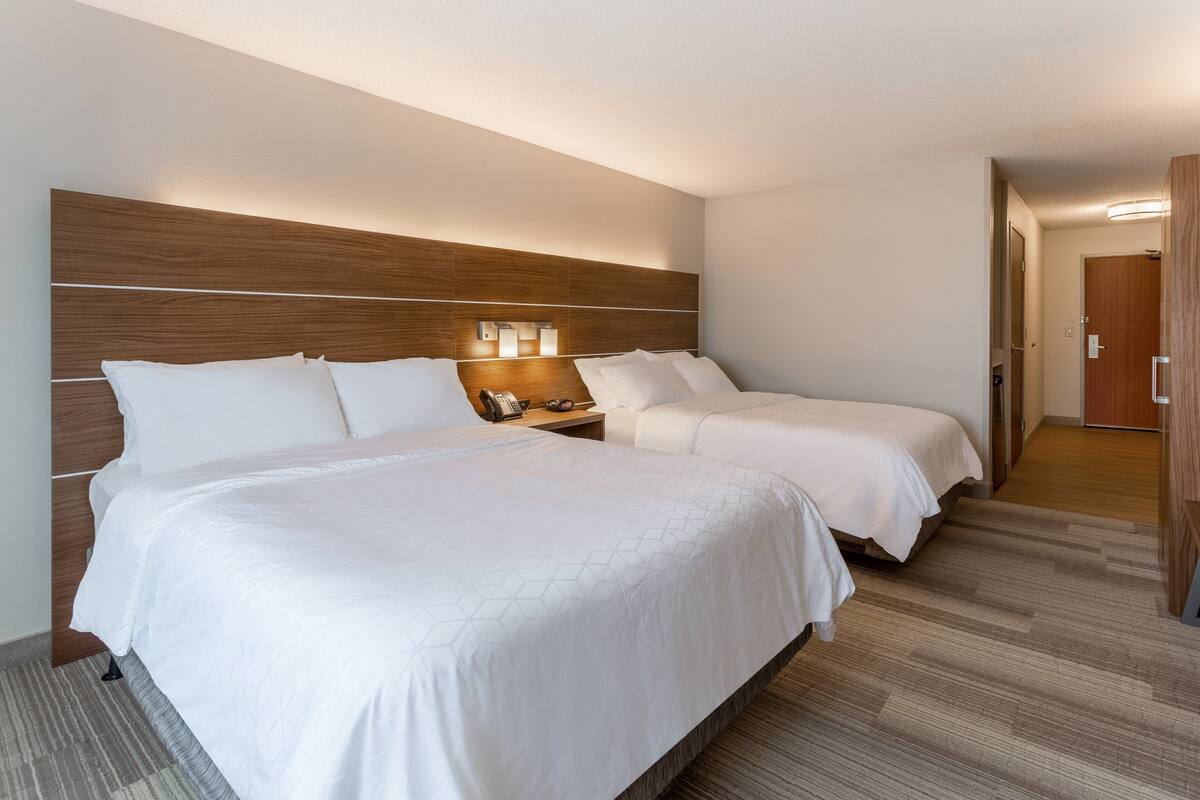 A hotel room with two beds, a wooden headboard, a nightstand with a phone, and a carpeted floor.