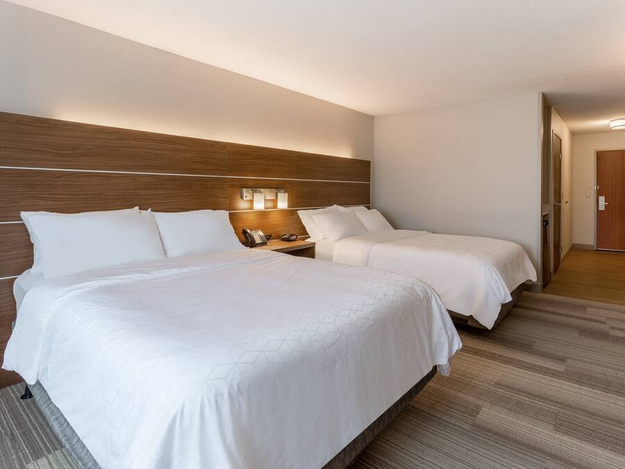A hotel room with two beds, a wooden headboard, a nightstand with a phone, and a carpeted floor.