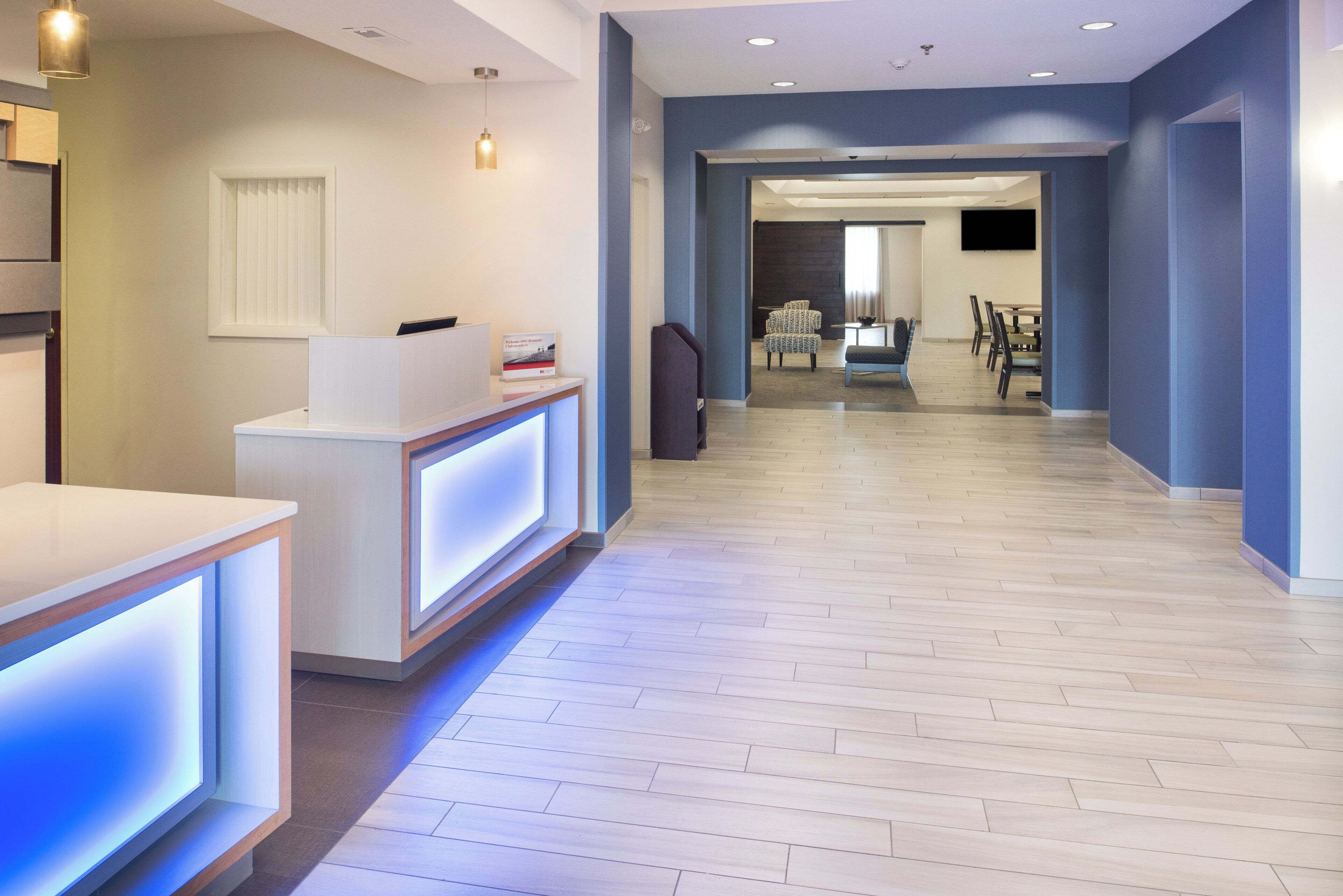 A modern hotel lobby with a reception desk, a seating area, and a dining space.