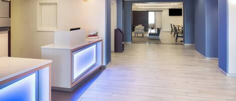 A modern hotel lobby with a reception desk, a seating area, and a dining space.