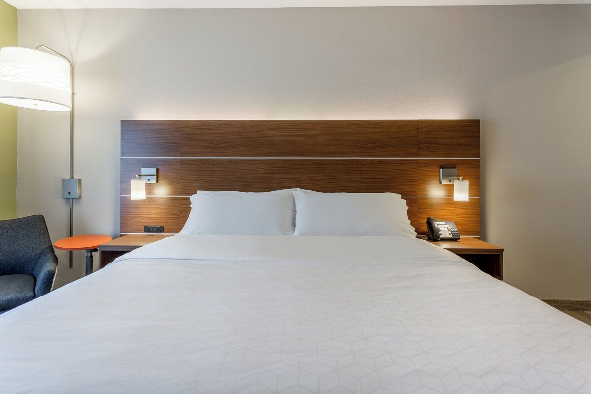 Une chambre d’hôtel avec un grand lit, deux tables de chevet, une chaise et une lampe.