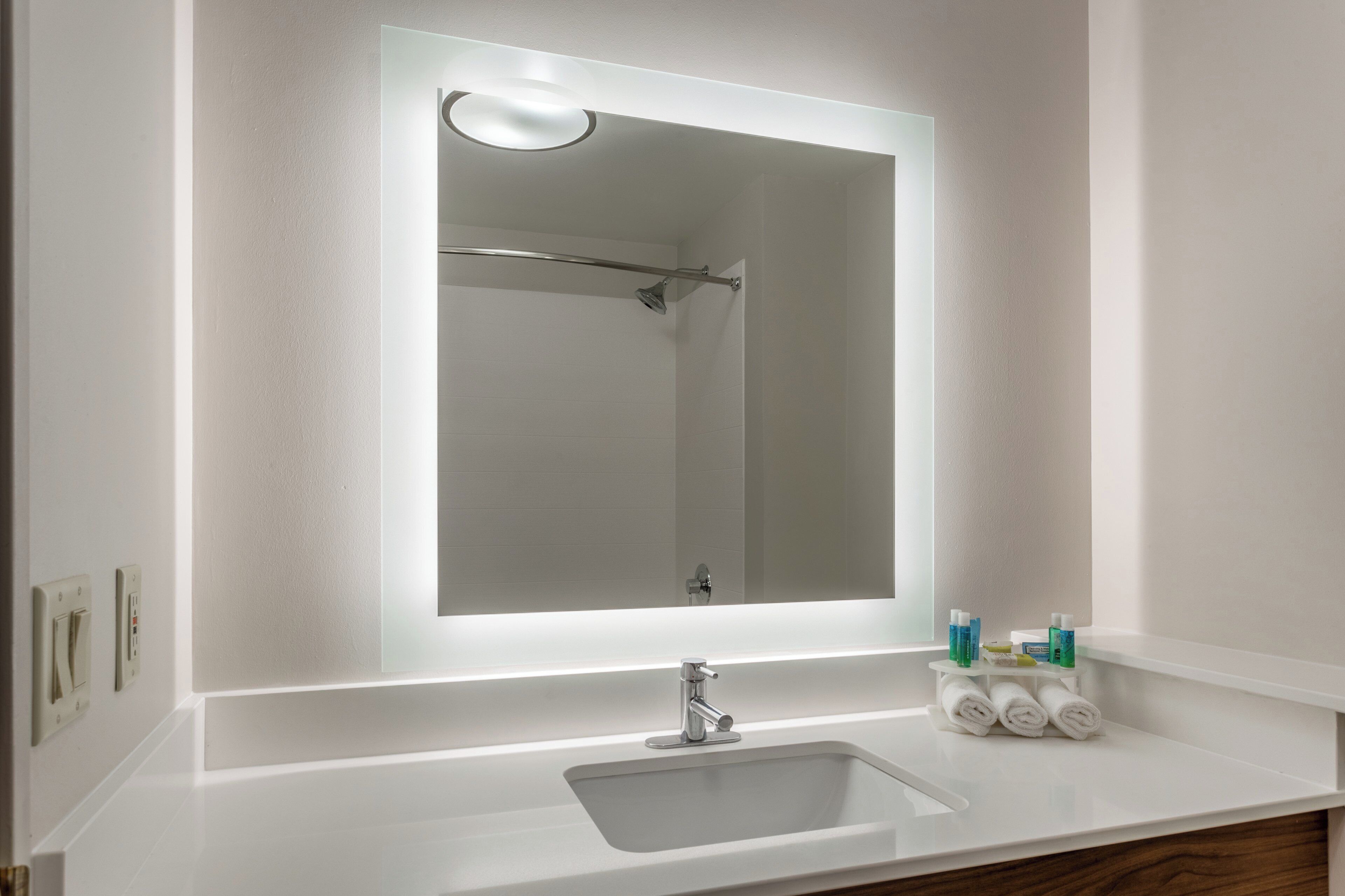 A bathroom with a large mirror, a sink, and toiletries.