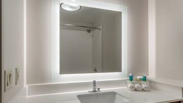 A bathroom with a large mirror, a sink, and toiletries.
