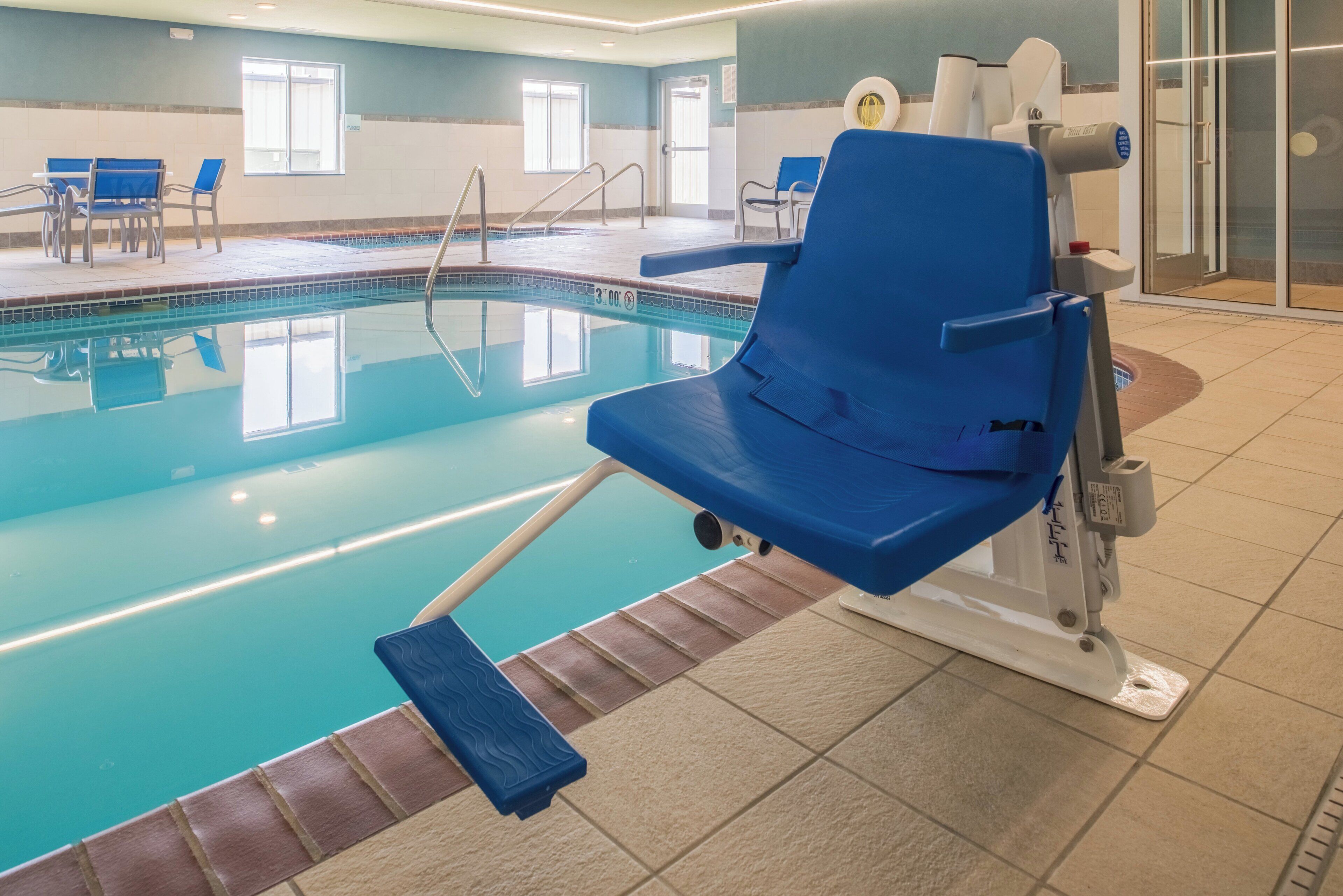 A pool area with a blue lounge chair, a diving board, and a tiled floor.