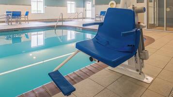 A pool area with a blue lounge chair, a diving board, and a tiled floor.
