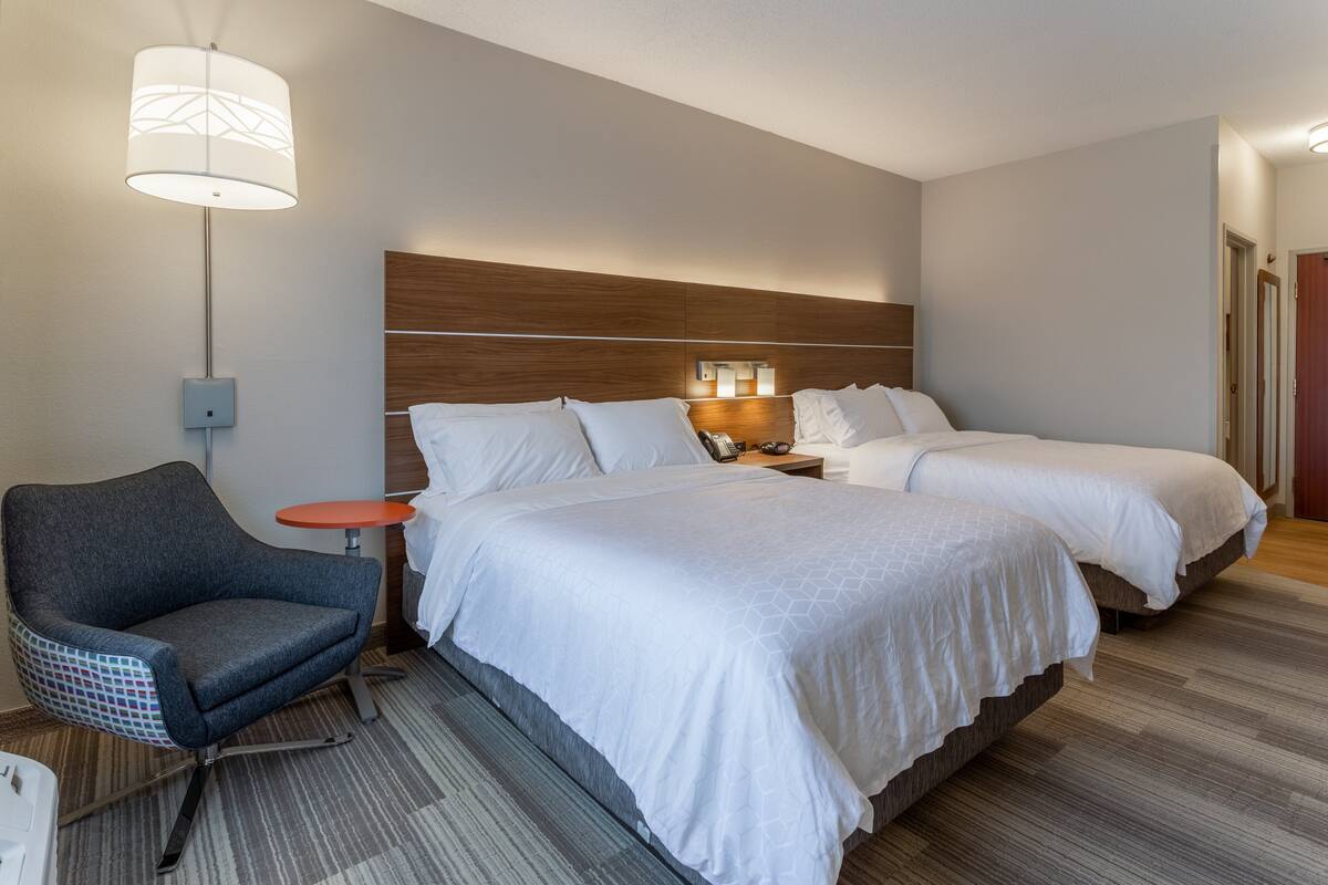A hotel room with two beds, a desk, a chair, a lamp, and a nightstand.