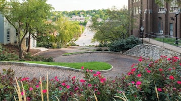 A paved courtyard with a curved walkway, surrounded by trees and flowering plants.
