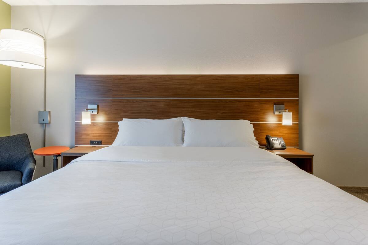 A hotel room with a large bed, a wooden headboard, two bedside tables with lamps, a chair, and a small table.