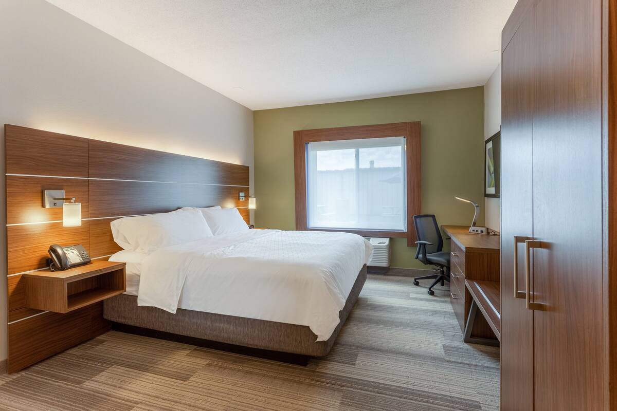 A hotel room with a large bed, bedside table with a phone, a desk with a chair, and a wardrobe.
