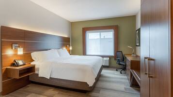 A hotel room with a large bed, bedside table with a phone, a desk with a chair, and a wardrobe.