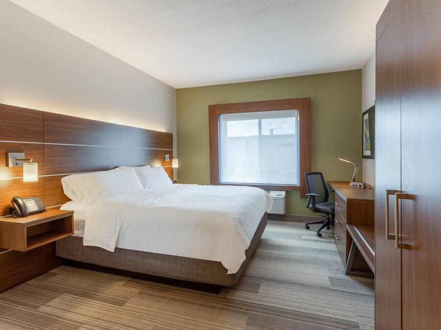 A hotel room with a large bed, bedside table with a phone, a desk with a chair, and a wardrobe.