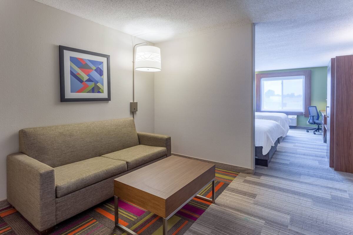 A hotel room with a sofa, a coffee table, a bed, a desk, and a window with a view.