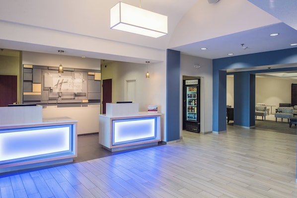 A hotel reception area with a modern design, including a reception desk, a beverage refrigerator, and a seating area with chairs. - Holiday Inn Express Hotel & Suites Burlington by IHG (Burlington)