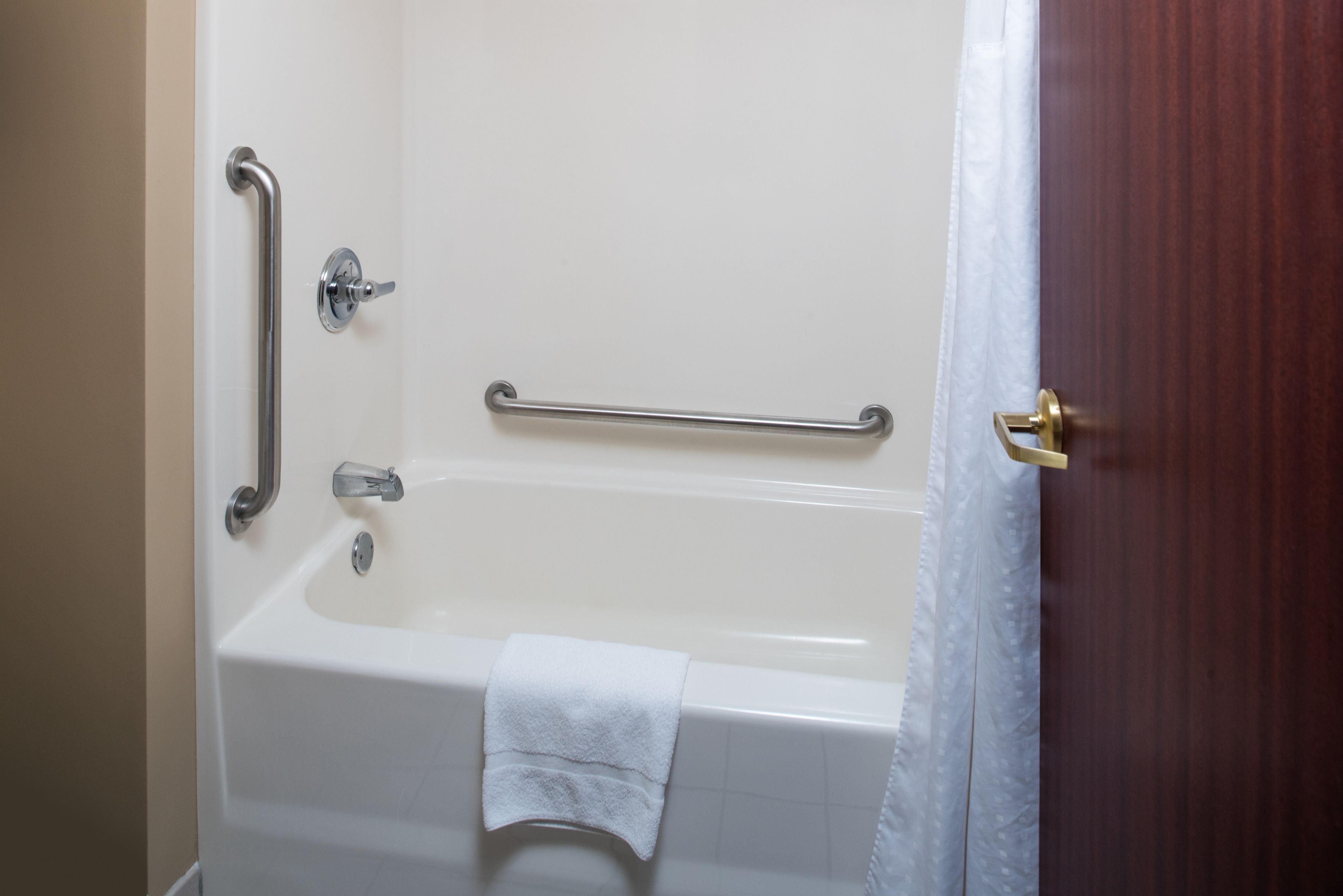 A bathroom with a white bathtub, grab bars, and a towel.