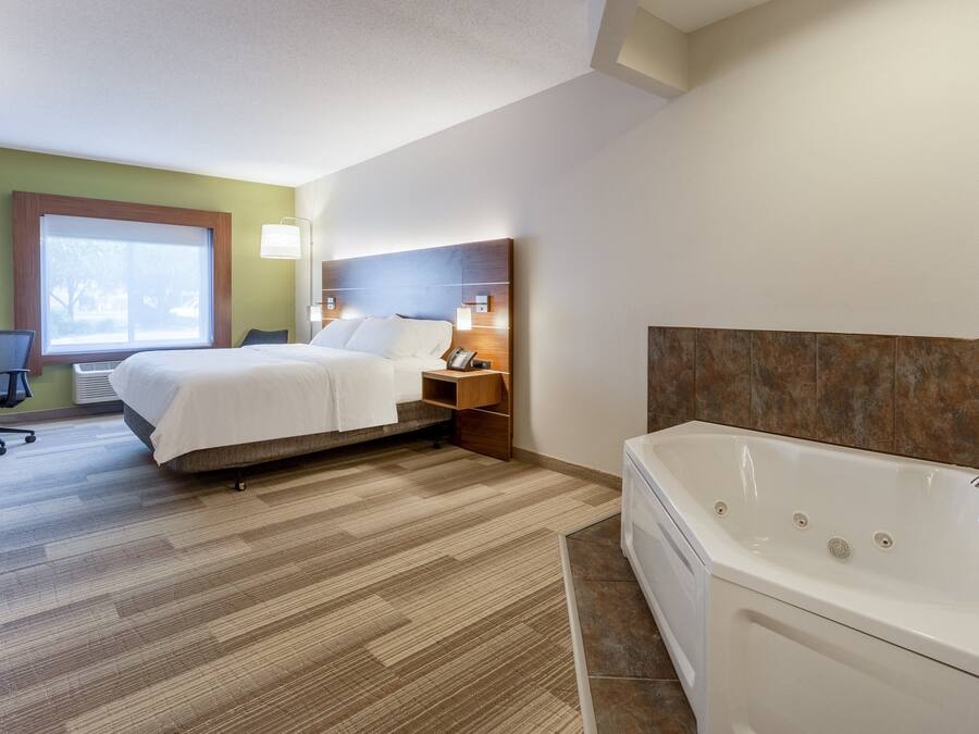 A hotel room with a bed, a desk, a chair, a window, and a bathtub.