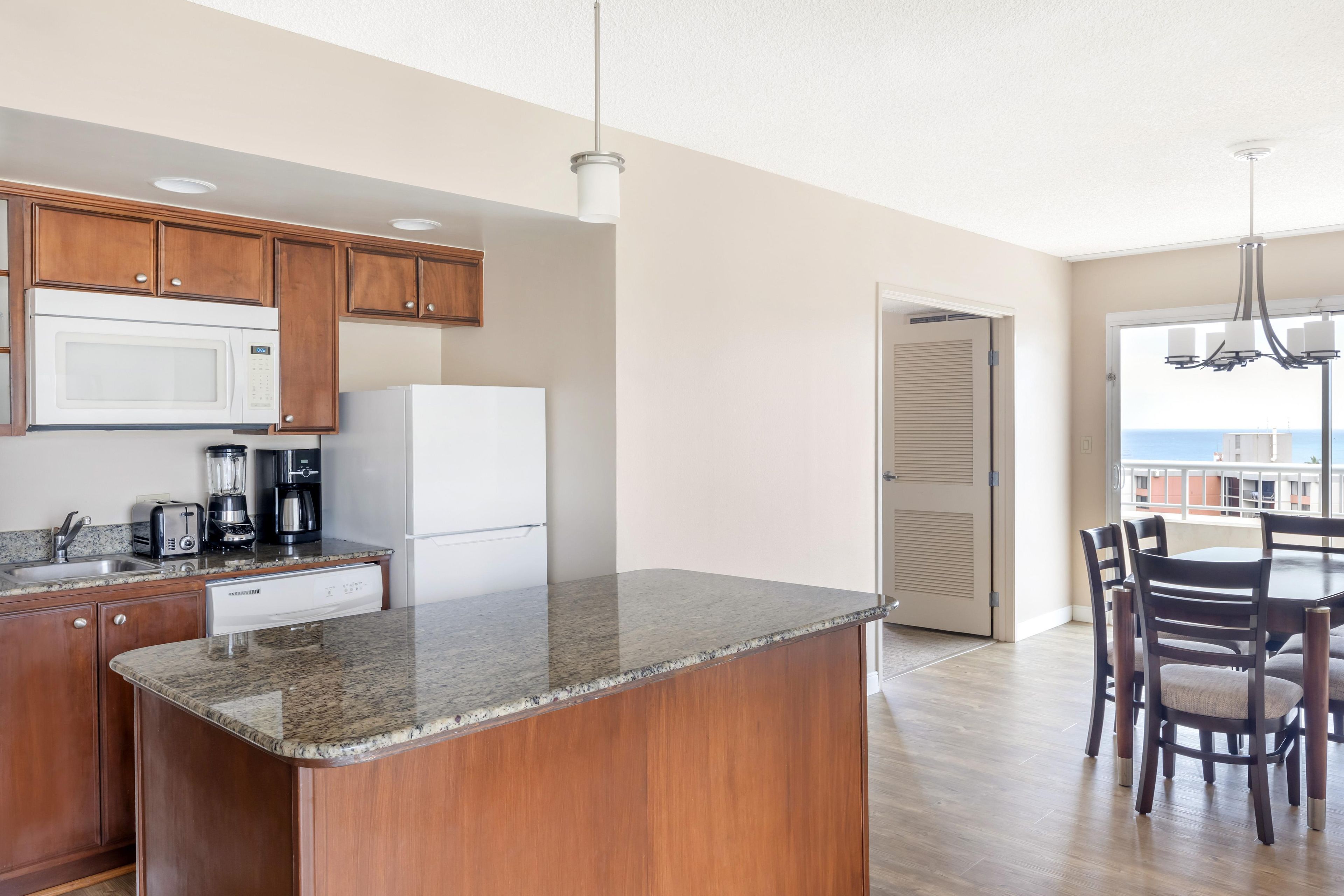 A modern kitchen with granite countertops, wooden cabinets, a built-in microwave, and a coffee maker.