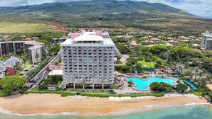 Un resort con una gran piscina, acceso directo a la playa y montañas al fondo.