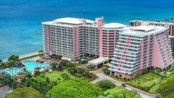 A multi-story hotel with a pool, surrounded by lush greenery and a view of the ocean.