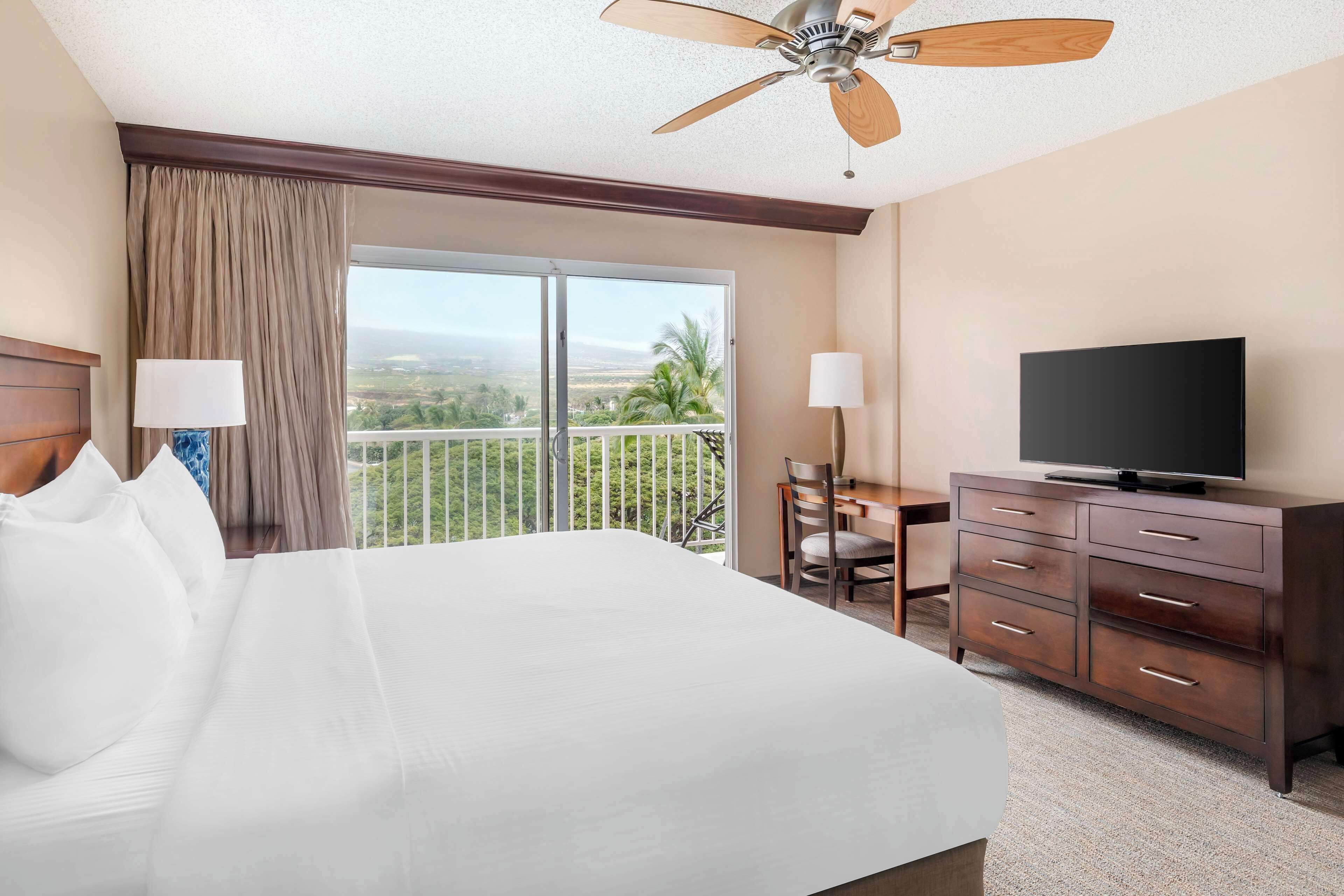 Habitación de hotel con una cama grande, televisión, escritorio y balcón con vistas al paisaje.