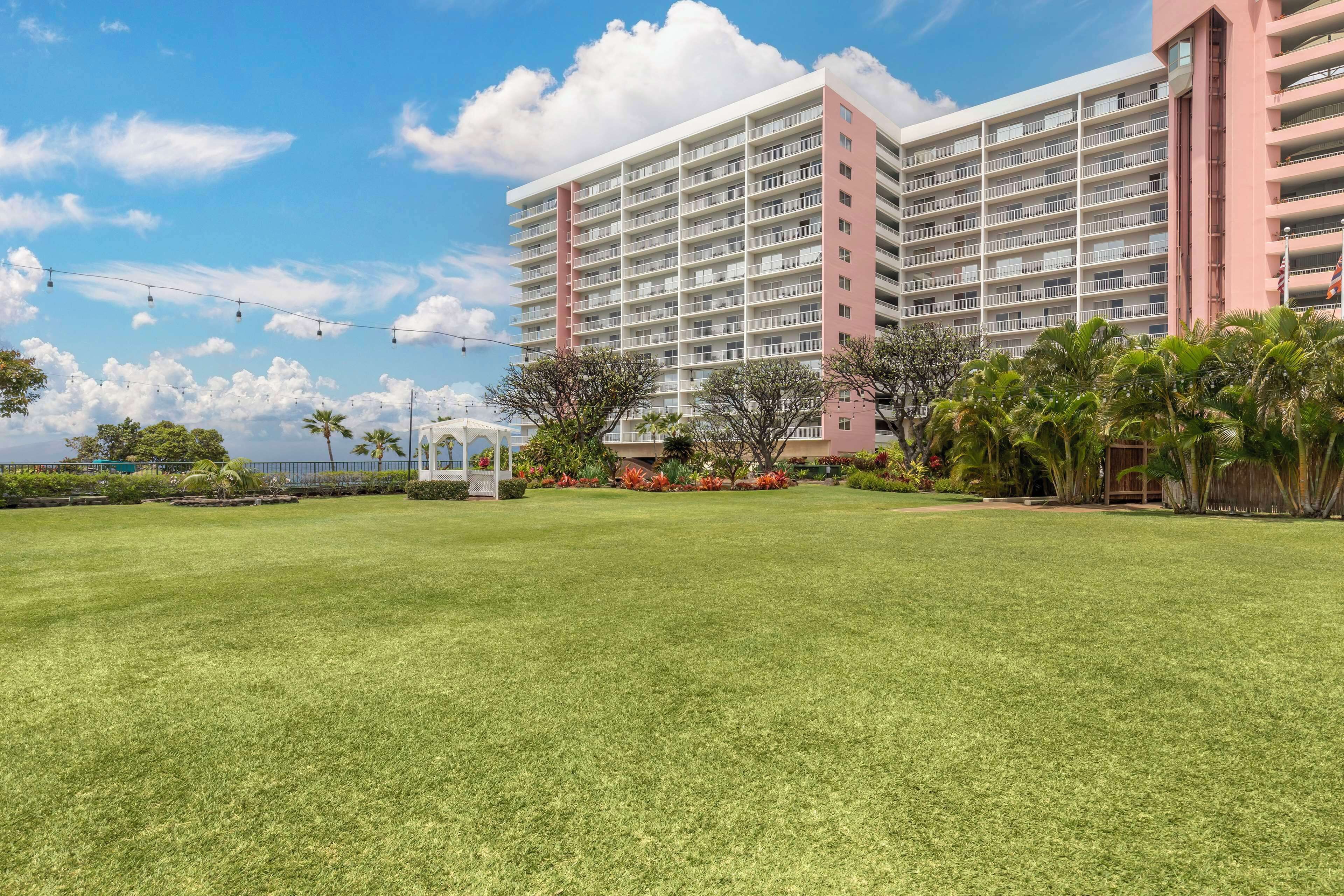 A multi-story hotel with a large lawn in the foreground, surrounded by palm trees and a gazebo.
