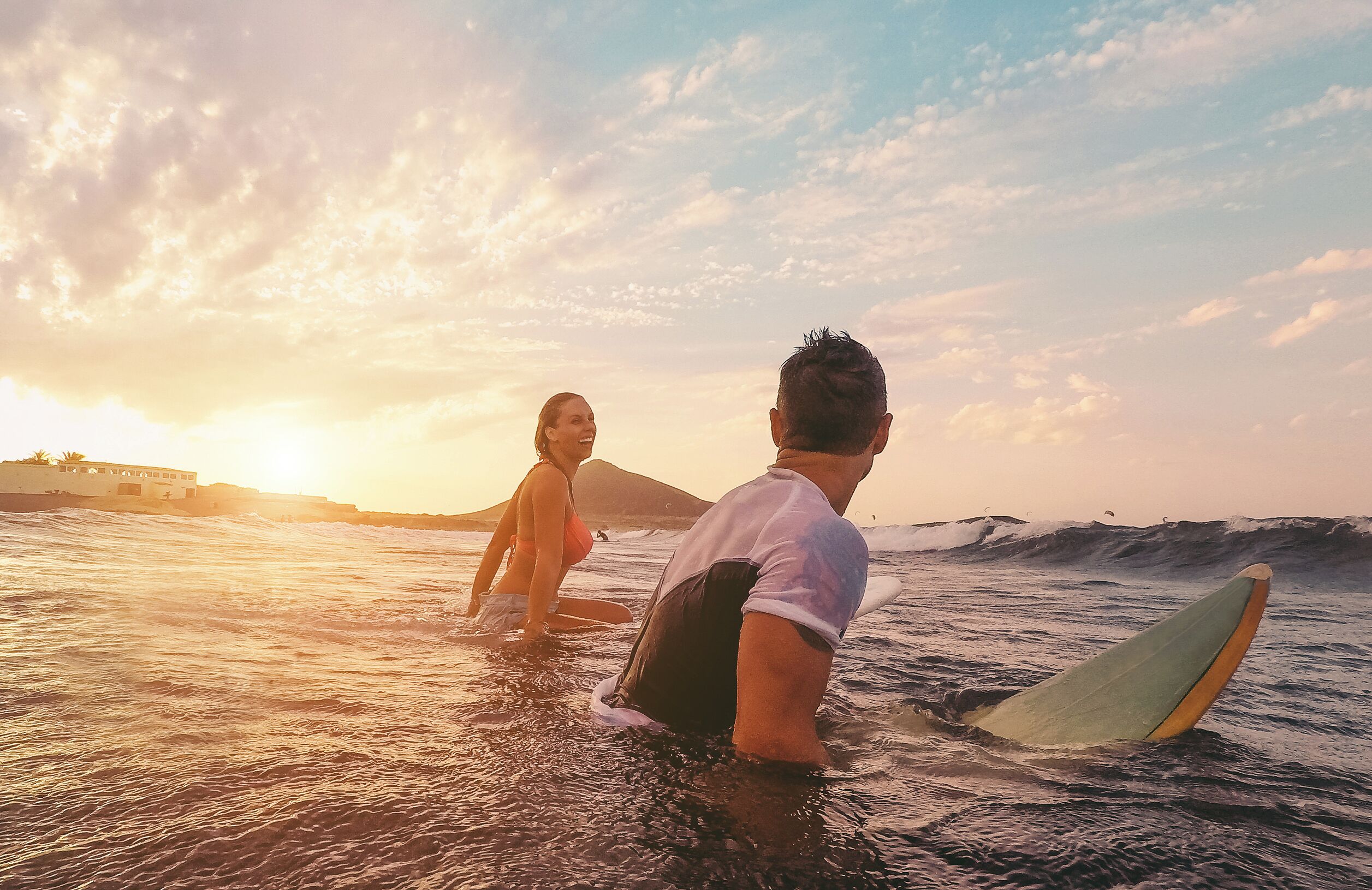Atardecer sobre el océano con gente en el agua y una tabla de surf.