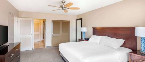 A hotel room with a bed, a TV, a dresser, a ceiling fan, and a door leading to a closet.