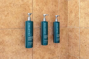 Drie flessen producten van Crabtree & Evelyn op een betegelde muur.
