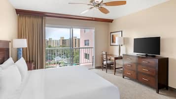 A hotel room with a large bed, a television, a desk, and a balcony with a view of buildings.