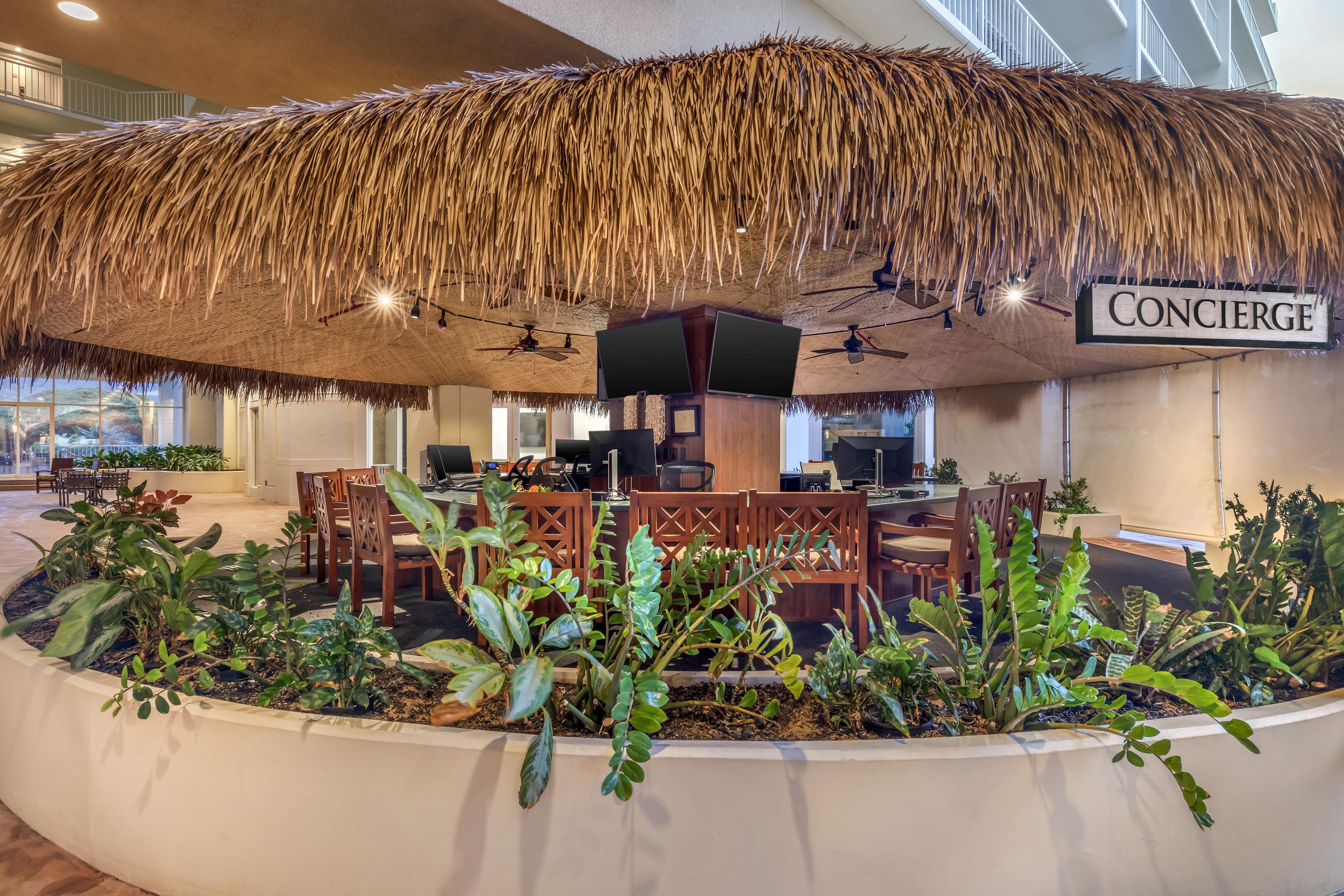 A restaurant area with a thatched roof, wooden furniture, and indoor plants.