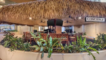 A restaurant area with a thatched roof, wooden furniture, and indoor plants.