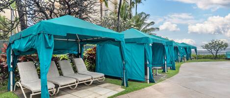 Des espaces extérieurs aménagés avec des chaises et des tables sous des auvents bleus, entourés de verdure et de palmiers.
