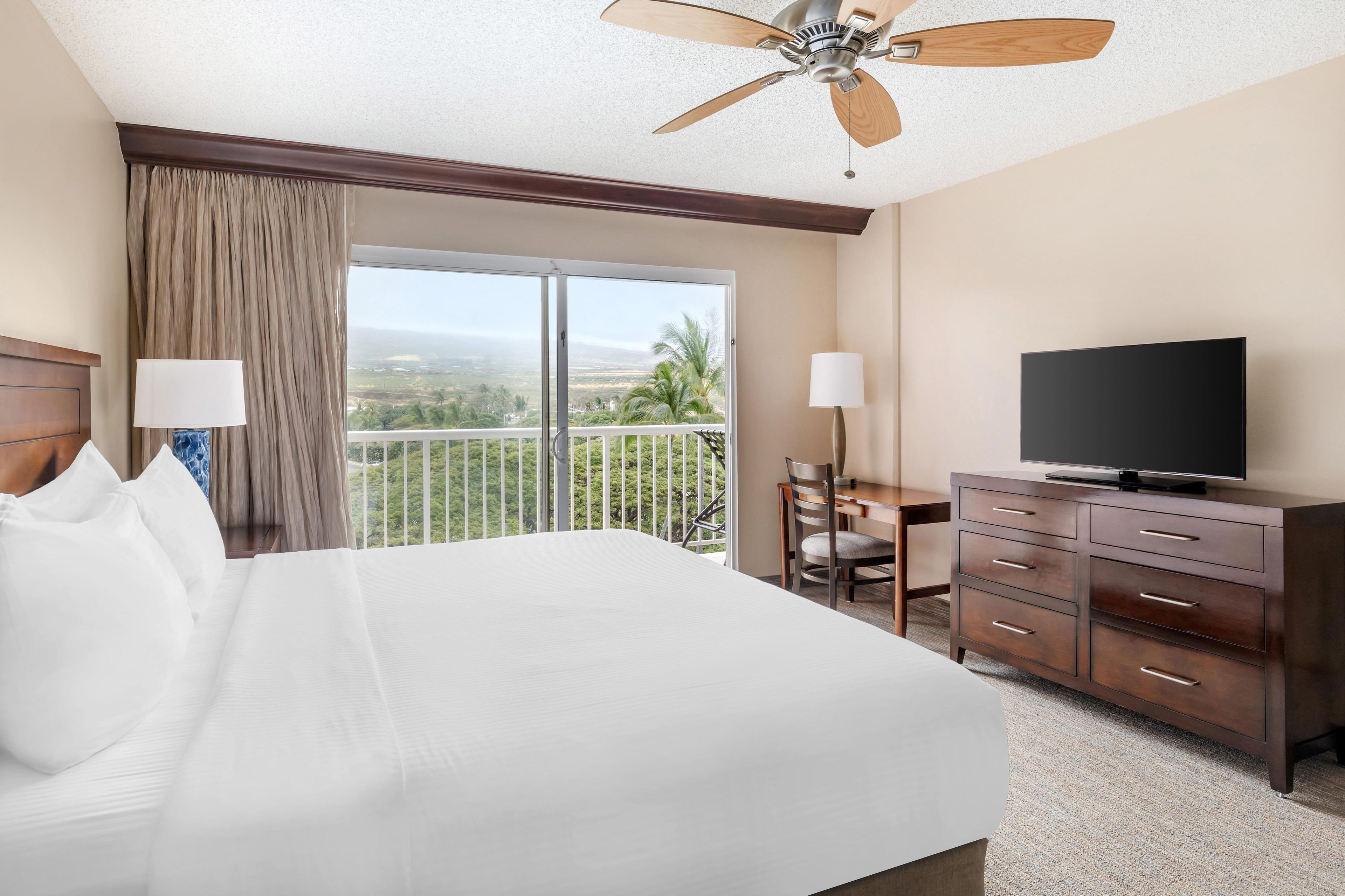 A hotel room with a bed, a desk, a television, and a balcony with a view.