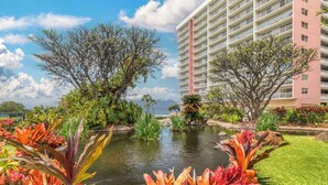 Un hotel con un edificio grande, un estanque y diversas plantas tropicales.