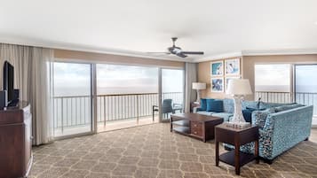 A hotel room with a balcony, a sofa set, a coffee table, a TV, and artwork on the wall.