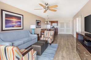 A living room with a sofa, armchairs, a coffee table, a TV, a ceiling fan, and a kitchen in the background. - Hilton Vacation Club Ka'anapali Beach Maui (Kaanapali)