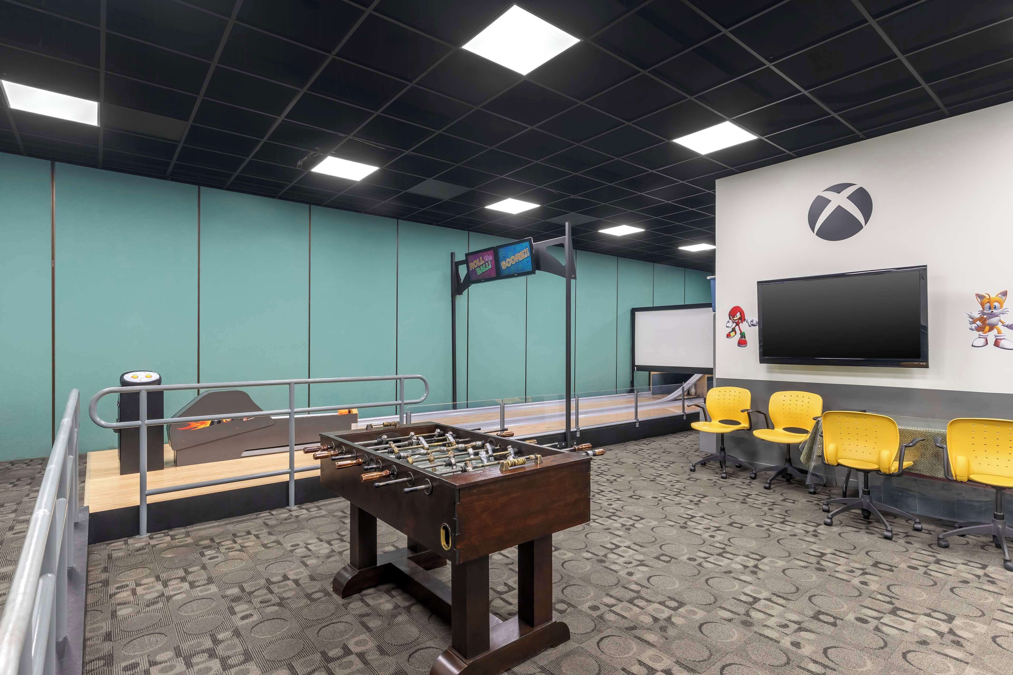A room with a foosball table, a flat-screen TV, and yellow chairs.