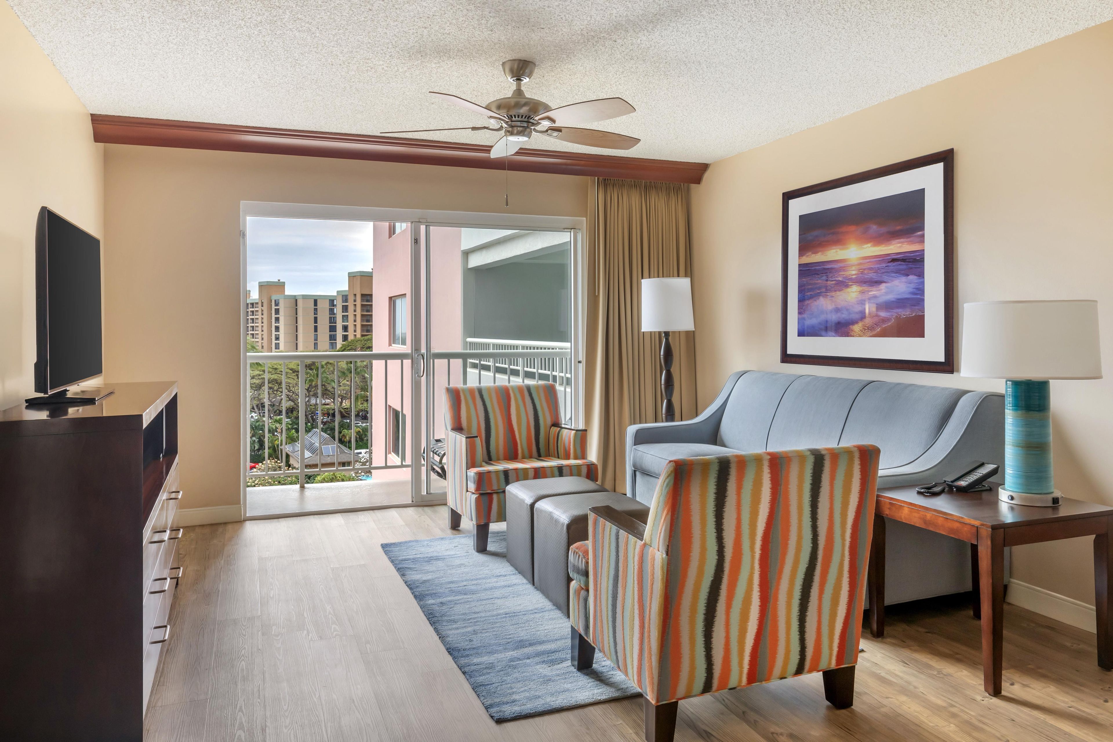 A hotel room with a balcony, a sofa, a TV, a lamp, and a painting.