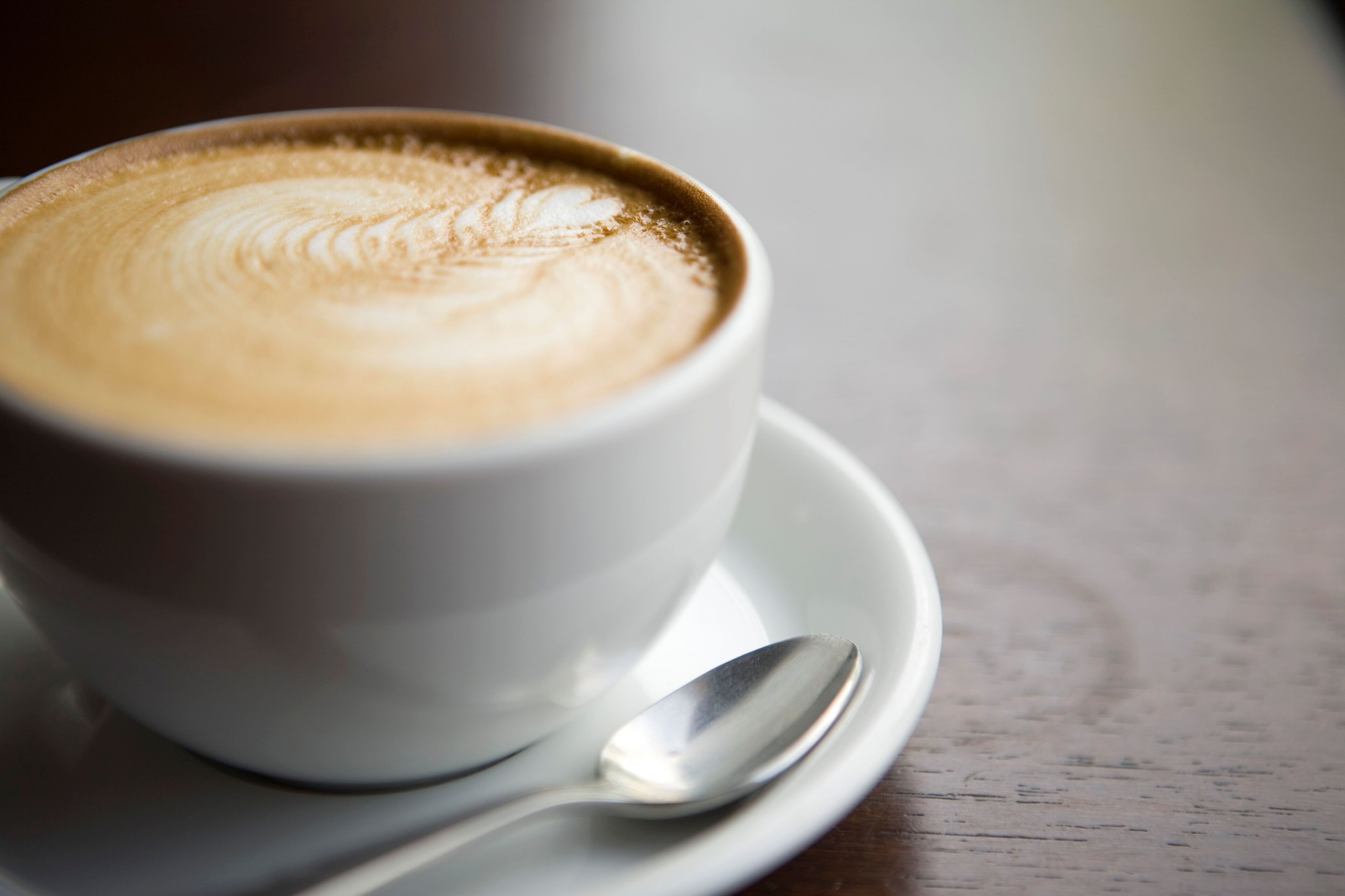 A cup of coffee with latte art on a saucer and a spoon beside it.