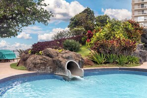 A swimming pool with a slide, surrounded by lush greenery and a rock formation. - Hilton Vacation Club Ka'anapali Beach Maui (Kaanapali)